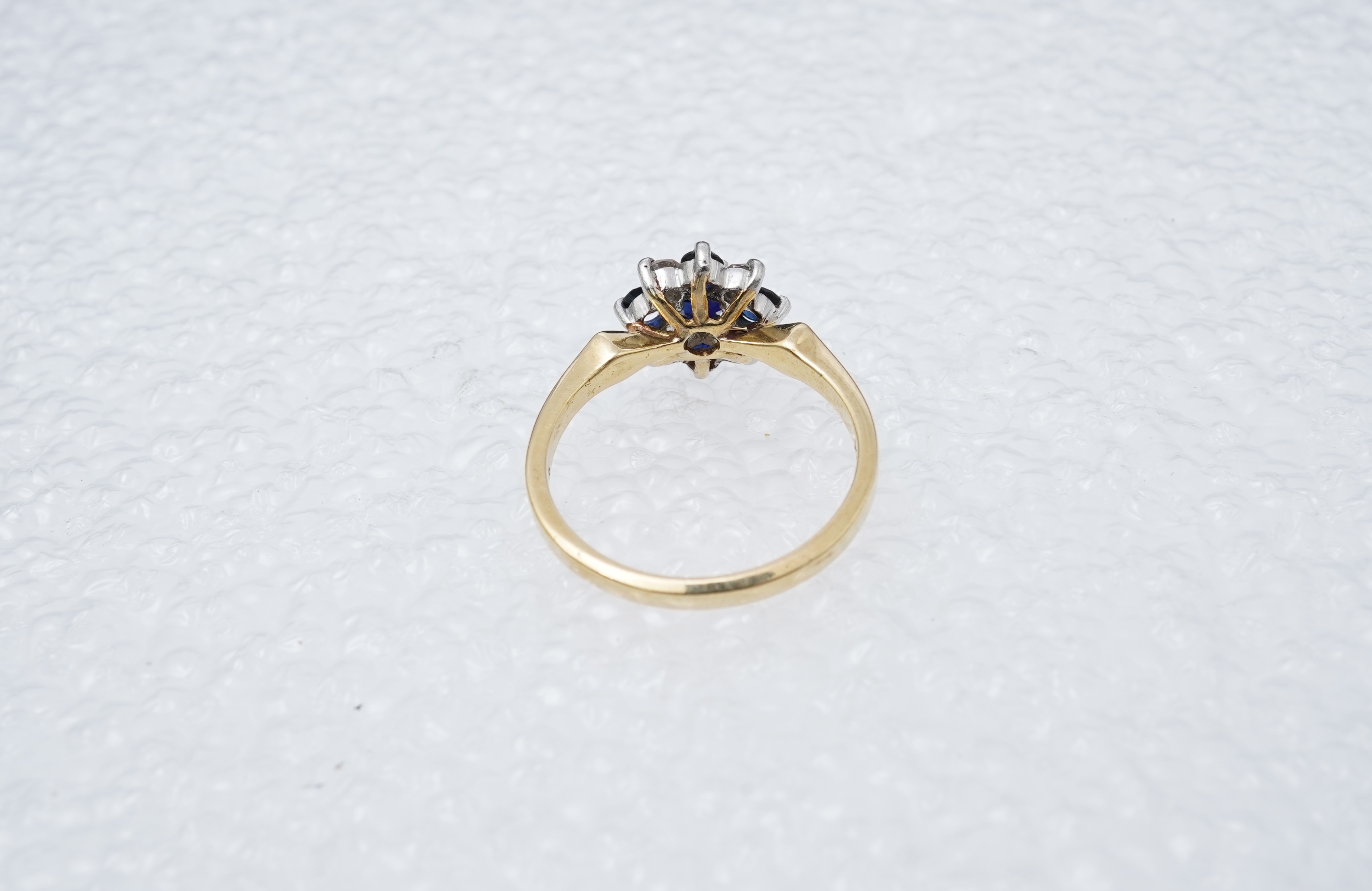 A sapphire and diamond cluster ring, set with circular-cut sapphires and brilliant-cut diamonds totalling approximately 0.20 carats, mounted in gold and platinum, size M, stamped 18CT PLAT, gross weight approximately 3.5